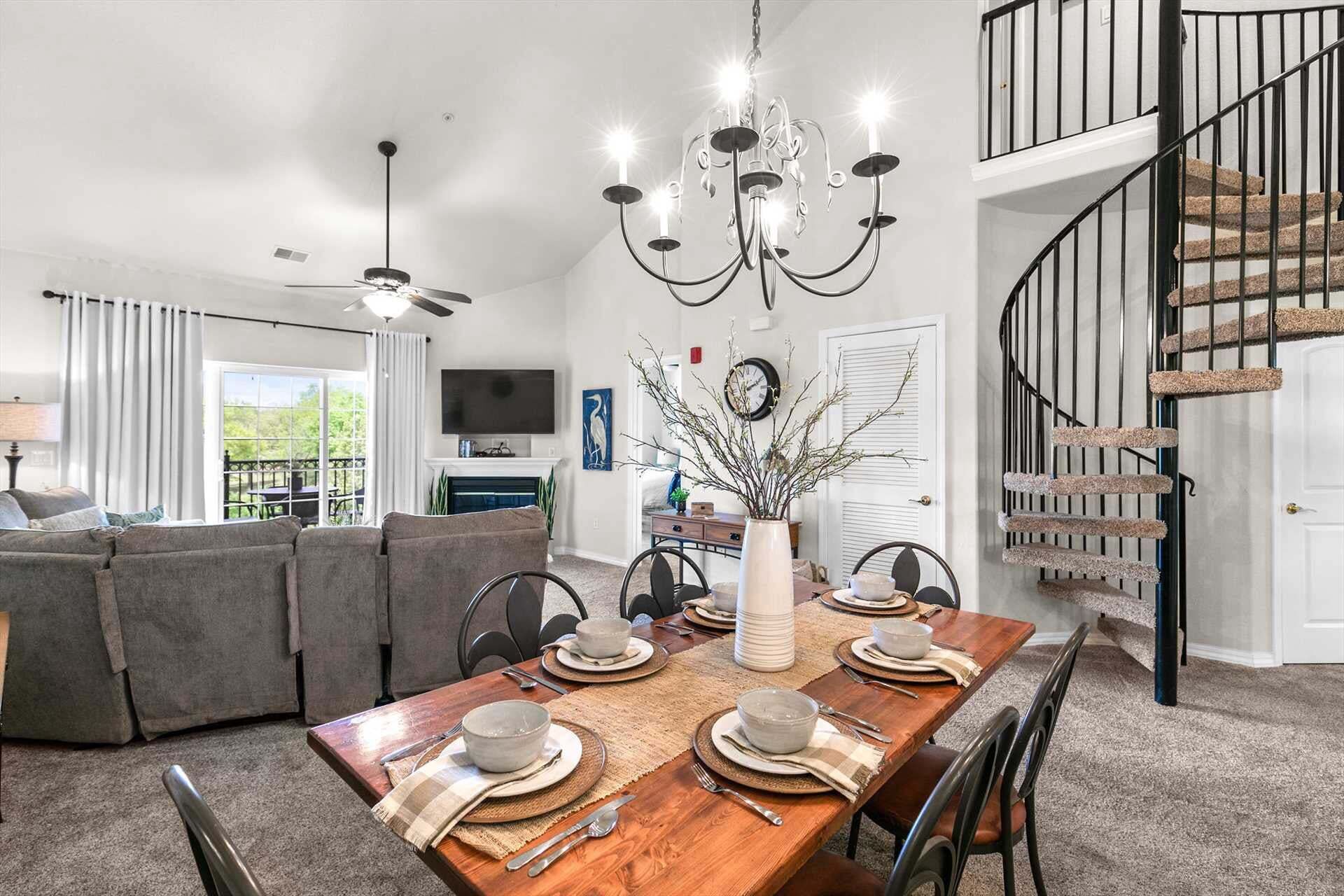 A dining area with a wooden table set for four, a chandelier, and a staircase with a cat tree.