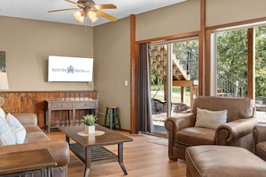 A spacious living room with a fireplace, a television mounted on the wall, and a large sliding glass door leading to an outdoor area. - Walk to Table Rock - Beautiful Logcabin- Free Daily Attraction Tickets (Branson)