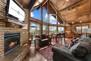 A spacious living room with a fireplace, a dining area, and a kitchen. - Walk to Table Rock - Beautiful Logcabin- Free Daily Attraction Tickets (Branson)