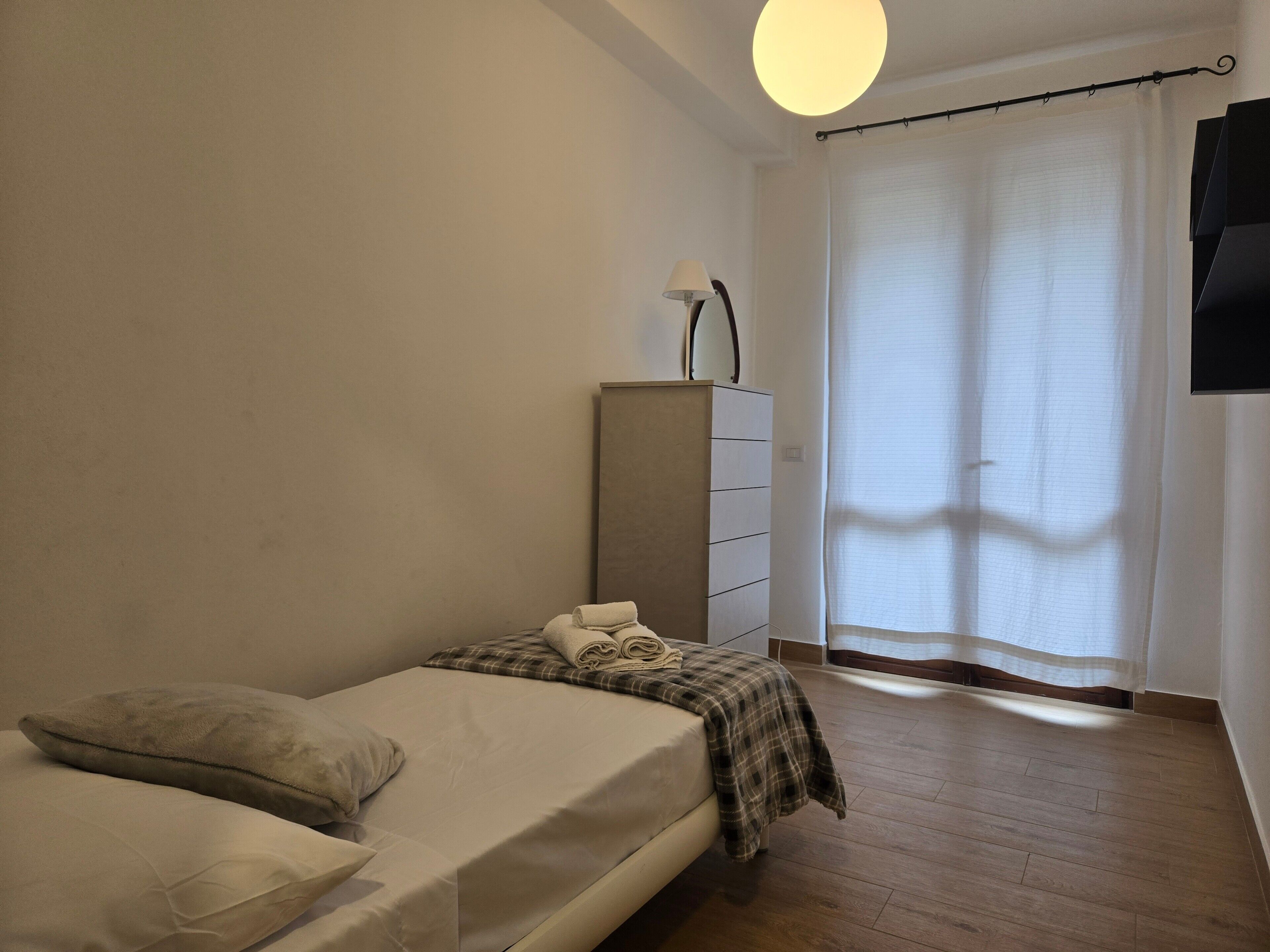 A bedroom with a bed, a dresser, a lamp, and a window with curtains.