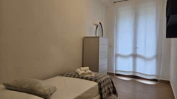 A bedroom with a bed, a dresser, a lamp, and a window with curtains.