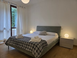 Une chambre d’hôtel avec un lit, deux tables de chevet, une fenêtre avec des rideaux et une vue sur la verdure.