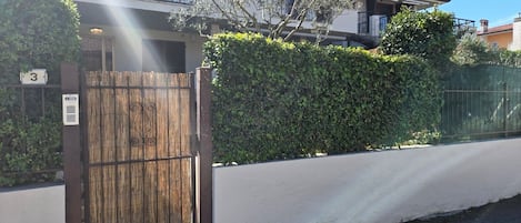 Un immeuble résidentiel doté d’une entrée sécurisée par un portail, d’une plaque indiquant le numéro de l’immeuble et d’une haie.