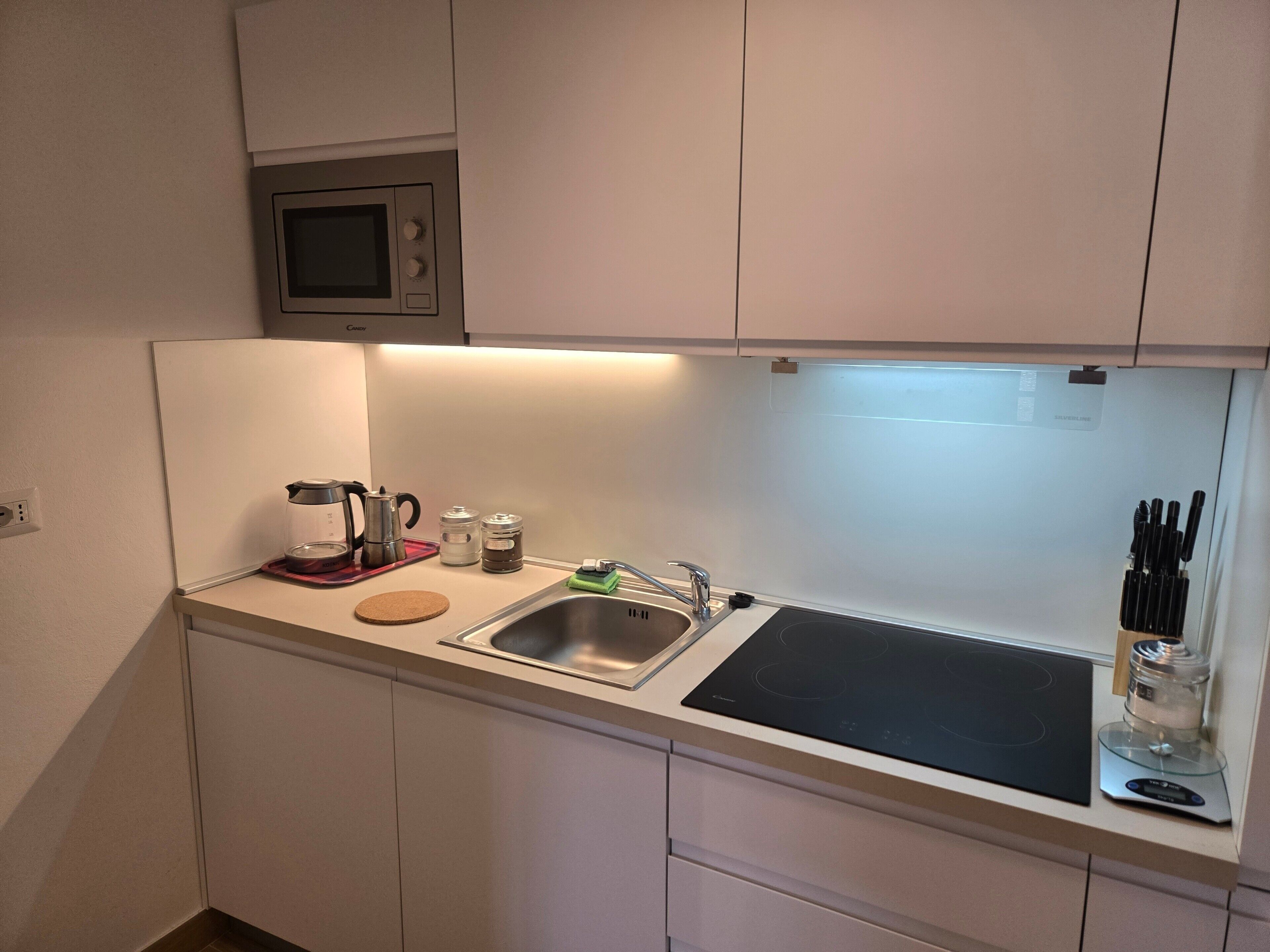 Cocina compacta con lavamanos, cafetera y bloque de cuchillos.
