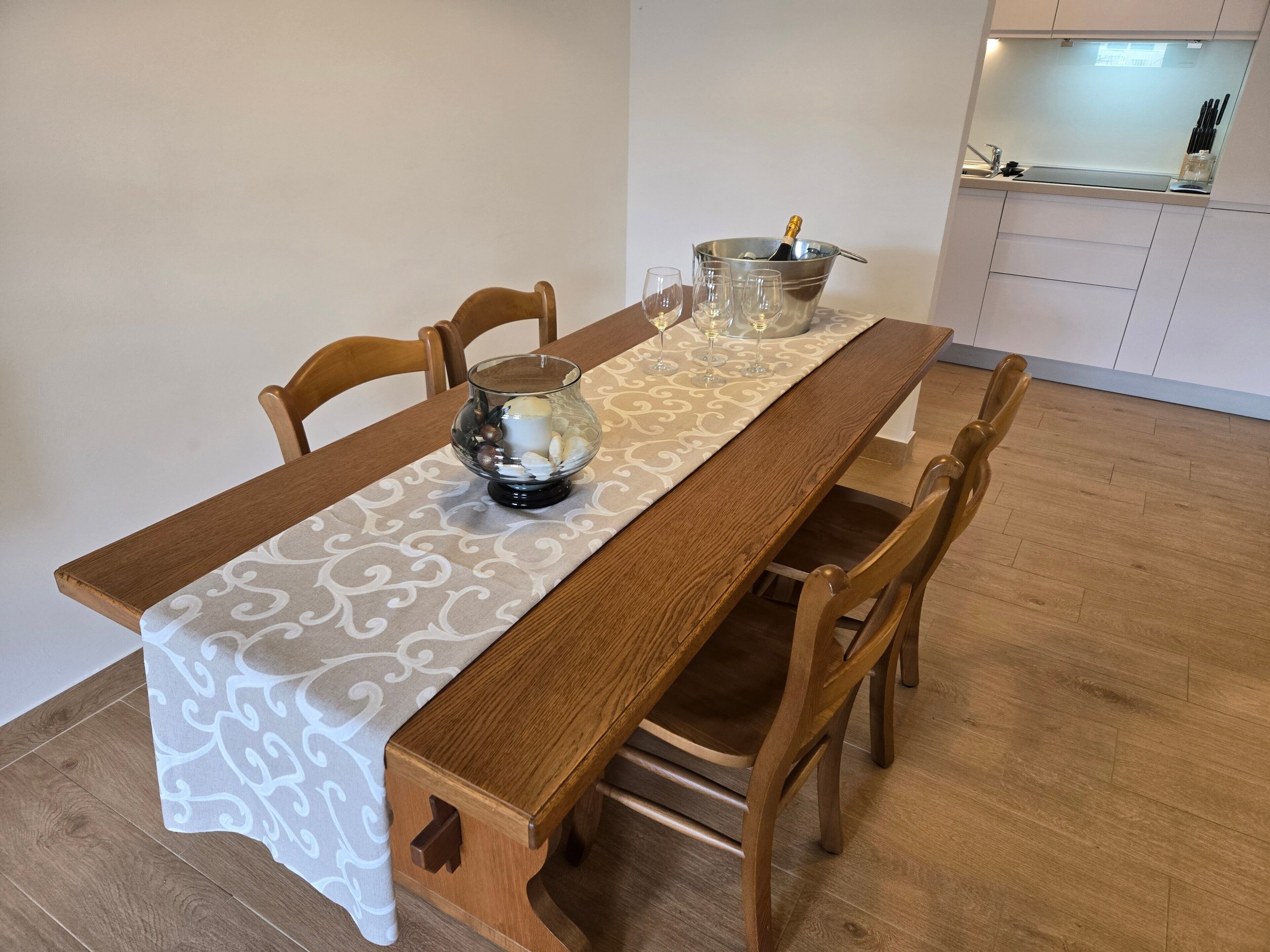 Una mesa de comedor con mantel estampado, seis sillas de madera y un centro de mesa con velas y un bol de vidrio.