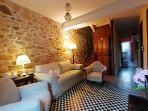 Ein Zimmer mit Steinwand, kariertem Boden, einer Couch, zwei Sesseln, einer Lampe und einer Treppe.