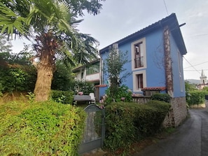 Ein zweistöckiges Gebäude mit blauer Fassade und Steinsockel, umgeben von Grünflächen und einem kleinen Garten.
