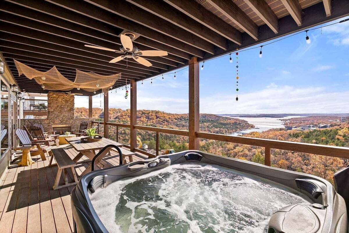 A hot tub on a wooden deck with a view of a lake and autumn foliage.