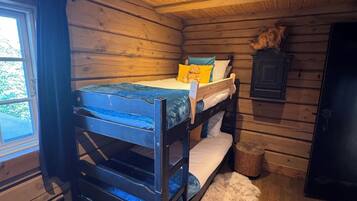 A bunk bed in a cabin with a wooden interior, a window, and a fur rug on the floor.