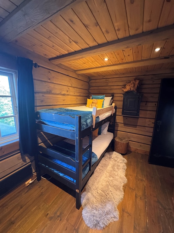 A bunk bed in a cabin with a wooden interior, a window, and a fur rug on the floor.