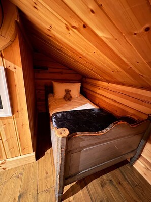 A wooden loft bedroom with a single bed, a teddy bear, and a window.