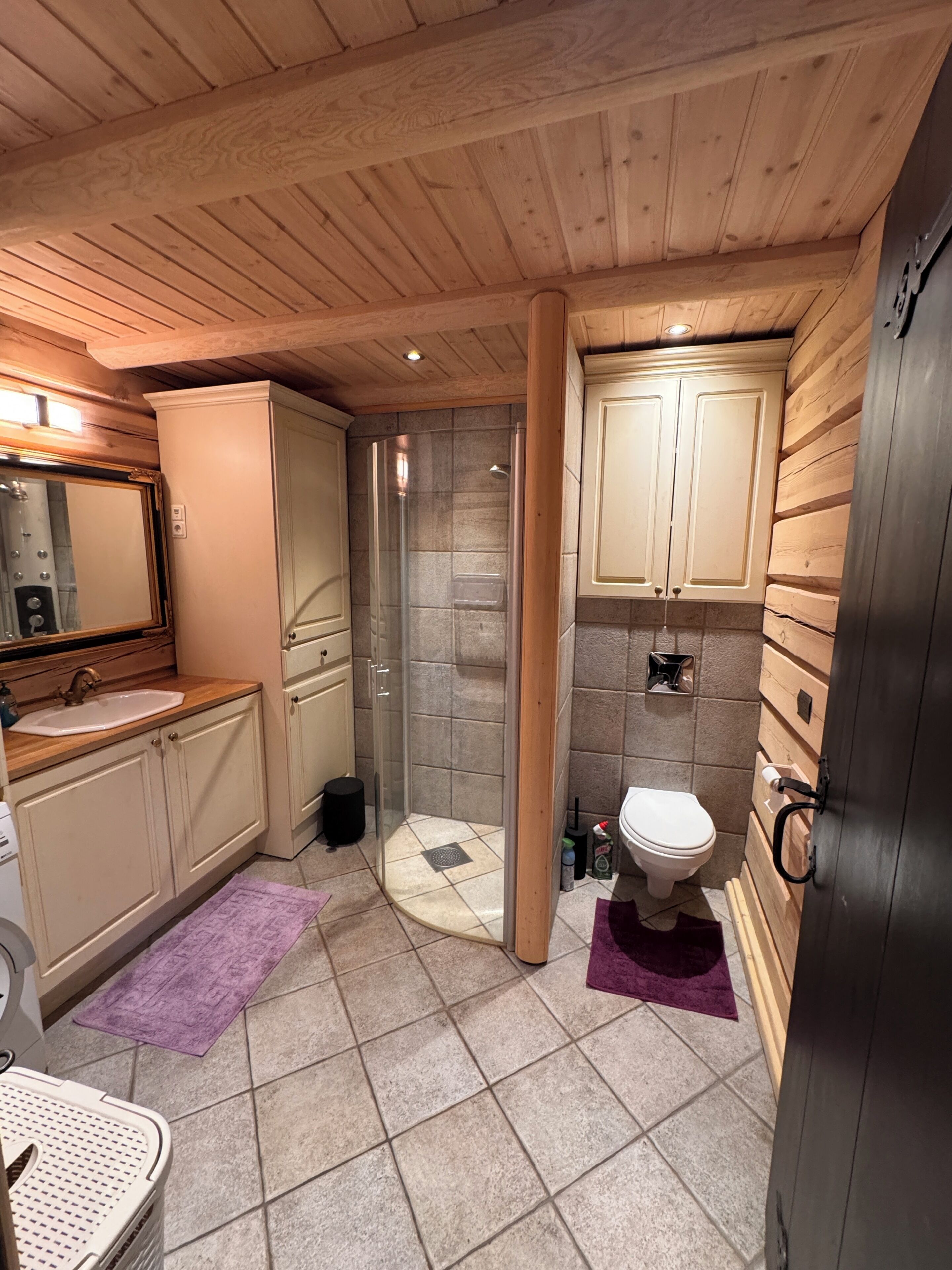 A bathroom with a wooden ceiling, a glass shower enclosure, a sink, and a toilet.