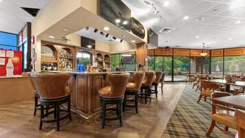 A bar area with a counter, stools, and a view through large windows.
