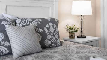 A neatly made bed with patterned pillows, a bedside table with a lamp and a small plant, and a white headboard.