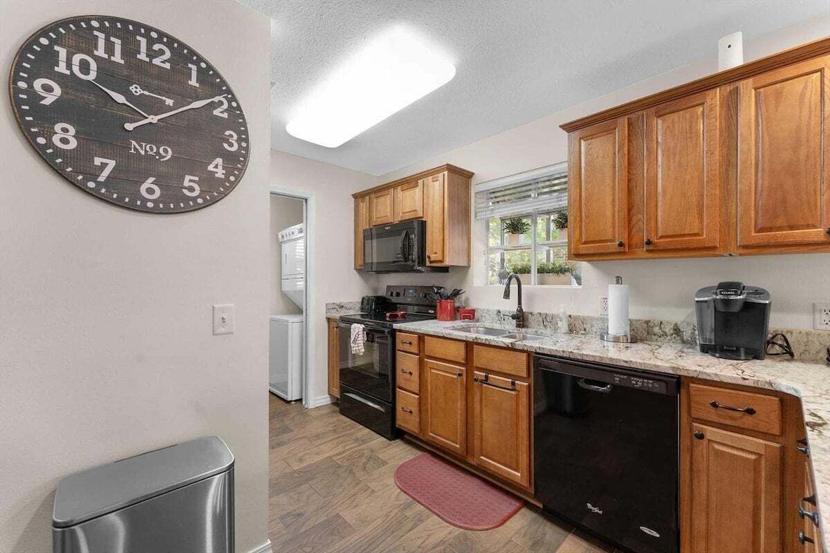 A kitchen with wooden cabinets, a stainless steel dishwasher, a microwave, and a clock on the wall.