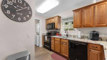 A kitchen with wooden cabinets, a stainless steel dishwasher, a microwave, and a clock on the wall.