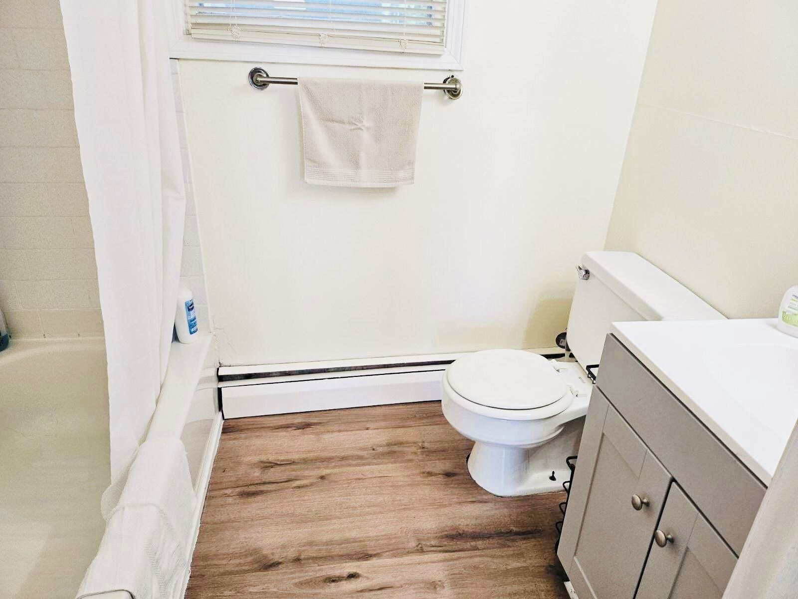 A small bathroom with a toilet, a shower curtain, and a wooden floor.