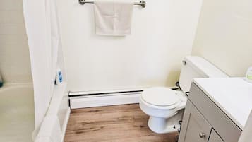 A small bathroom with a toilet, a shower curtain, and a wooden floor.