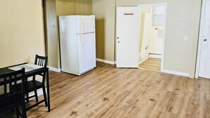 A room with a wooden floor, a white refrigerator, a dining table with chairs, and a door leading to another room. - Nice apartment near Whole Foods, Brown University, Downtown, Hospitals (Providence)