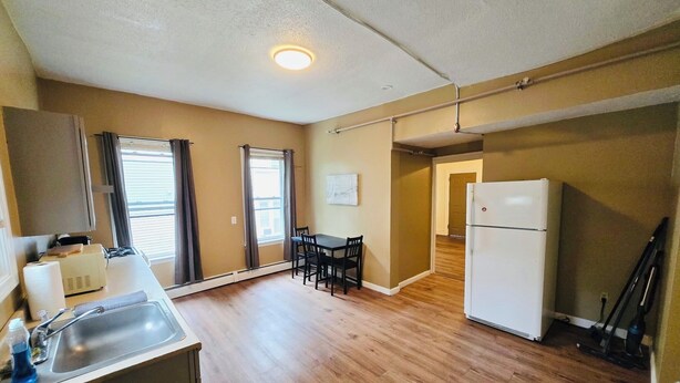 A compact kitchen with a sink, a refrigerator, and a dining area with a table and chairs. - Nice apartment near Whole Foods, Brown University, Downtown, Hospitals (Providence)