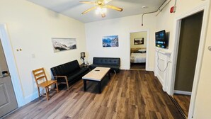 A living room with a sofa, a coffee table, a wooden chair, a ceiling fan, and a television. - Nice apartment near Whole Foods, Brown University, Downtown, Hospitals (Providence)