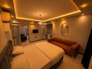 A modern bedroom with a large bed, a sofa, a TV, and a mirror. - Yazıcı Rezidans Keçiören (Ankara)