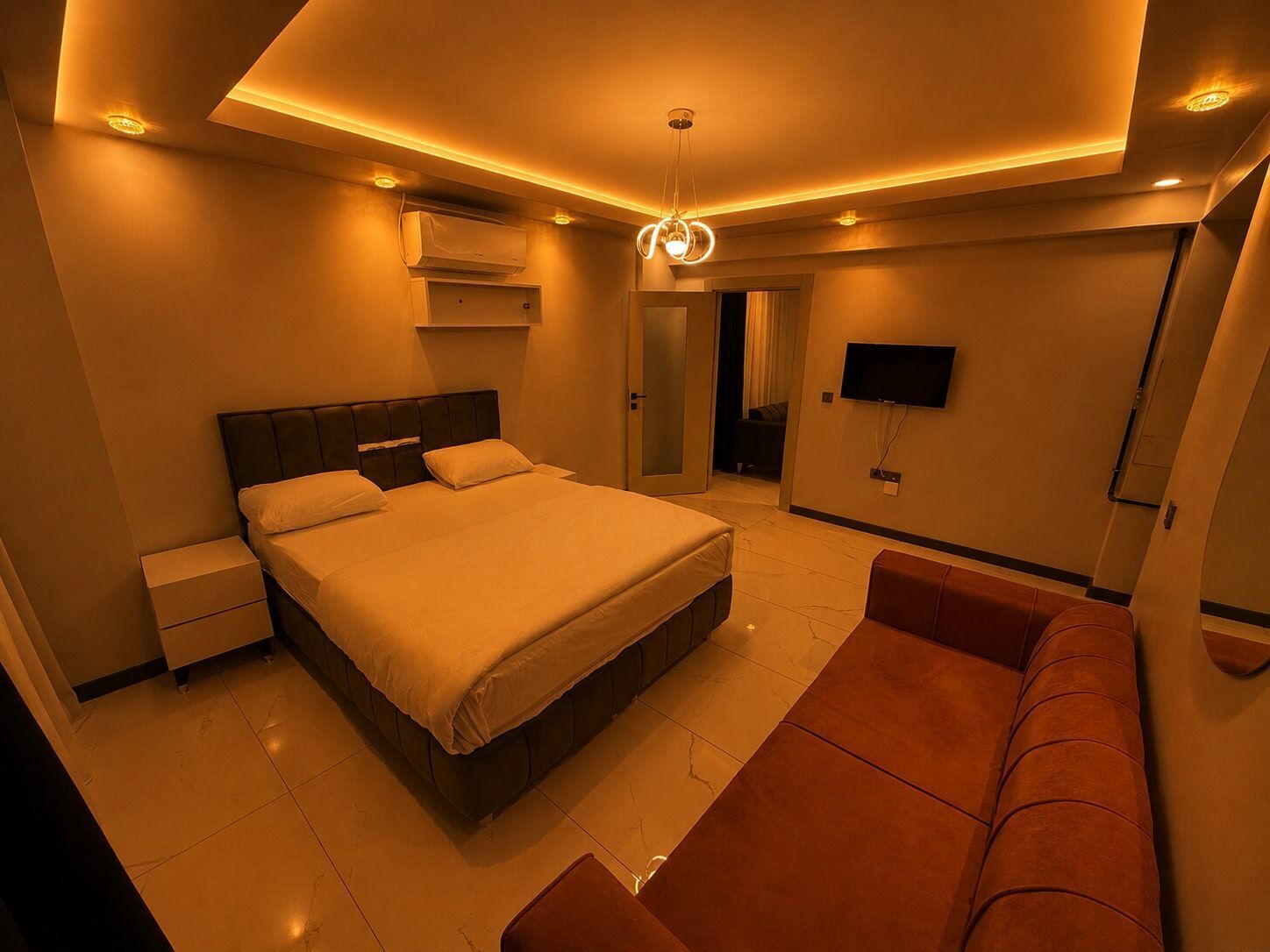 A modern bedroom with a large bed, a flat-screen TV, and a sofa.