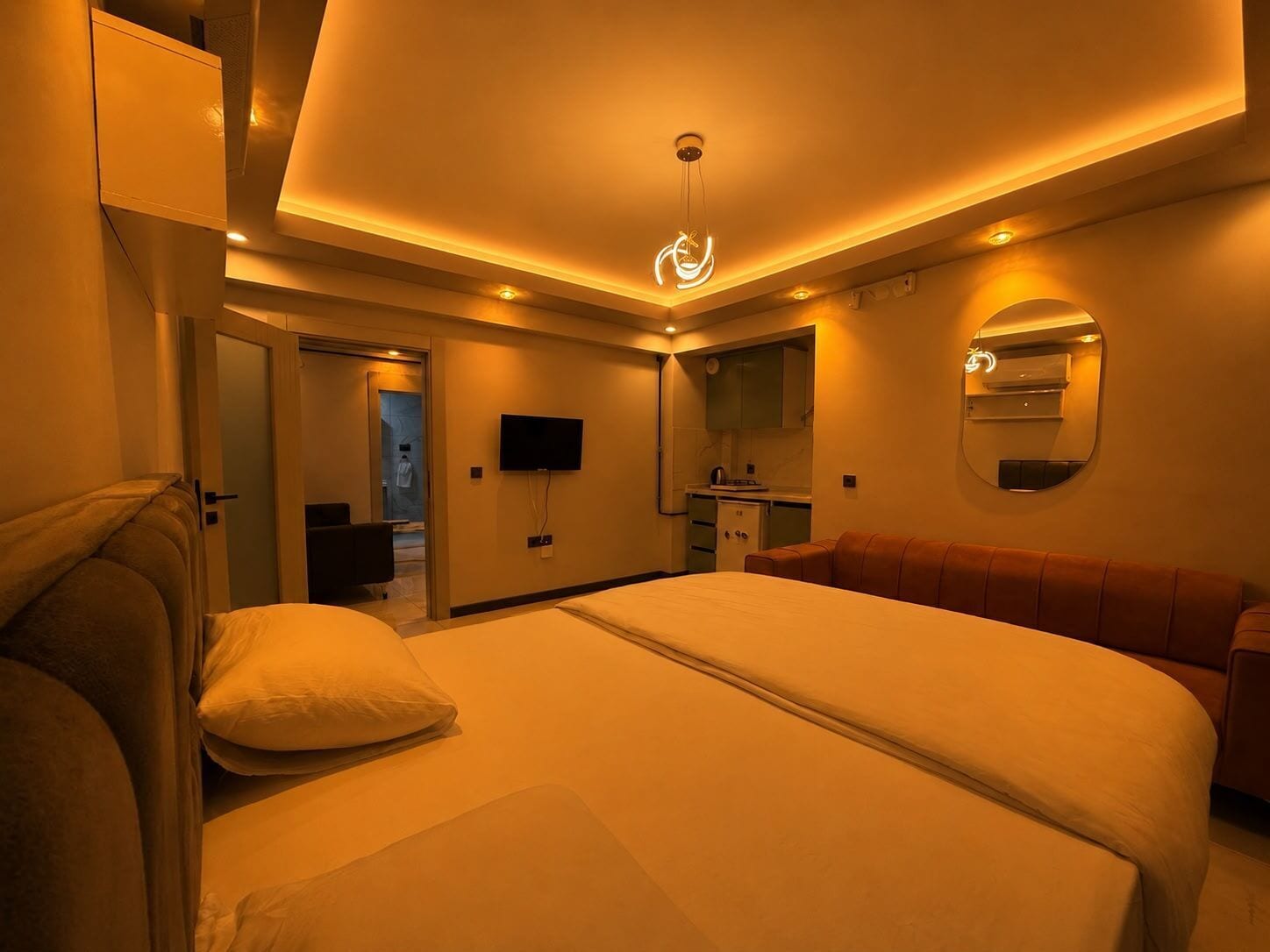 A hotel room with a bed, a seating area, a television, a mirror, and a door leading to a bathroom.