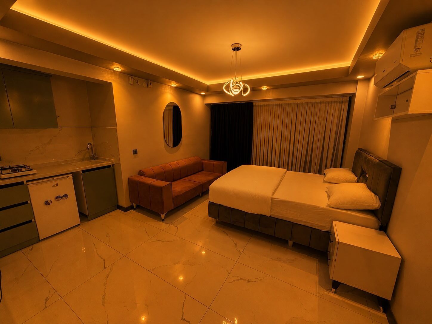 Een moderne hotelkamer met een kitchenette, een bank, een bed met hoofdeinde en een klein nachtkastje.