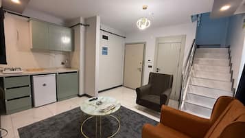 Una sala de estar moderna con un sofá, una mesa de centro, una zona de cocina con armarios y una escalera.