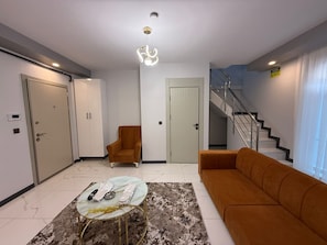 A modern living room with a sofa, armchair, coffee table, and a staircase. - Yazıcı Rezidans Keçiören (Ankara)
