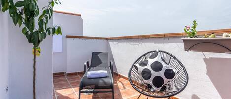 Una terraza en la azotea con una tumbona, un sillón colgante y un limonero en maceta.