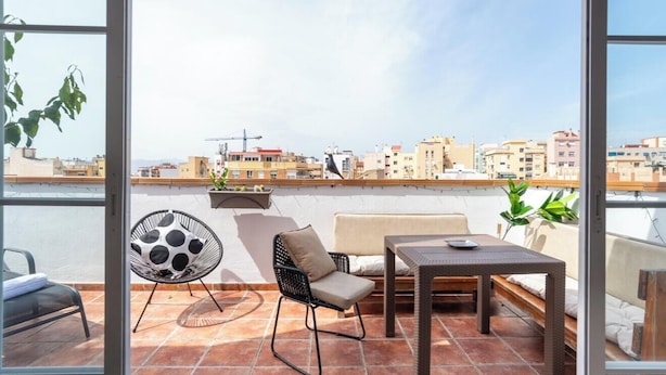 Uma varanda com sofá, poltrona, mesa e vista para a cidade.