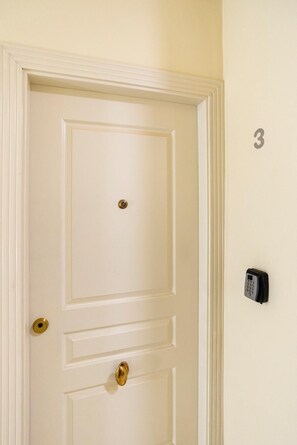 A white door with a brass doorknob and a keyhole, a wall-mounted intercom, and a number '3' on the wall. - New GR3 Penthouse Apartment in Downtown Málaga with a Cozy Terrace (Málaga)