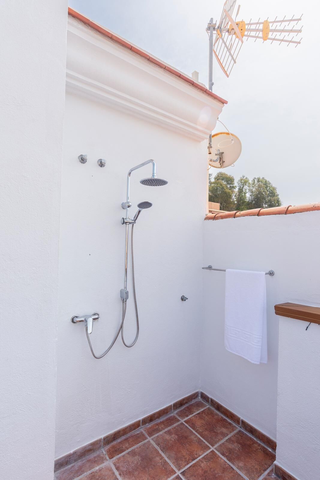 A small, enclosed shower area with a white wall, a tiled floor, and a towel rack.