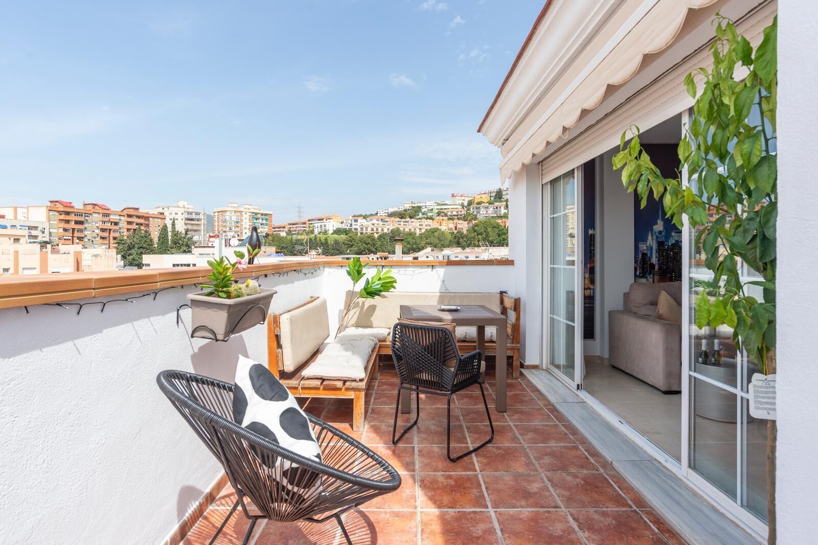 A terrace with outdoor furniture, a view of the city, and a potted plant.