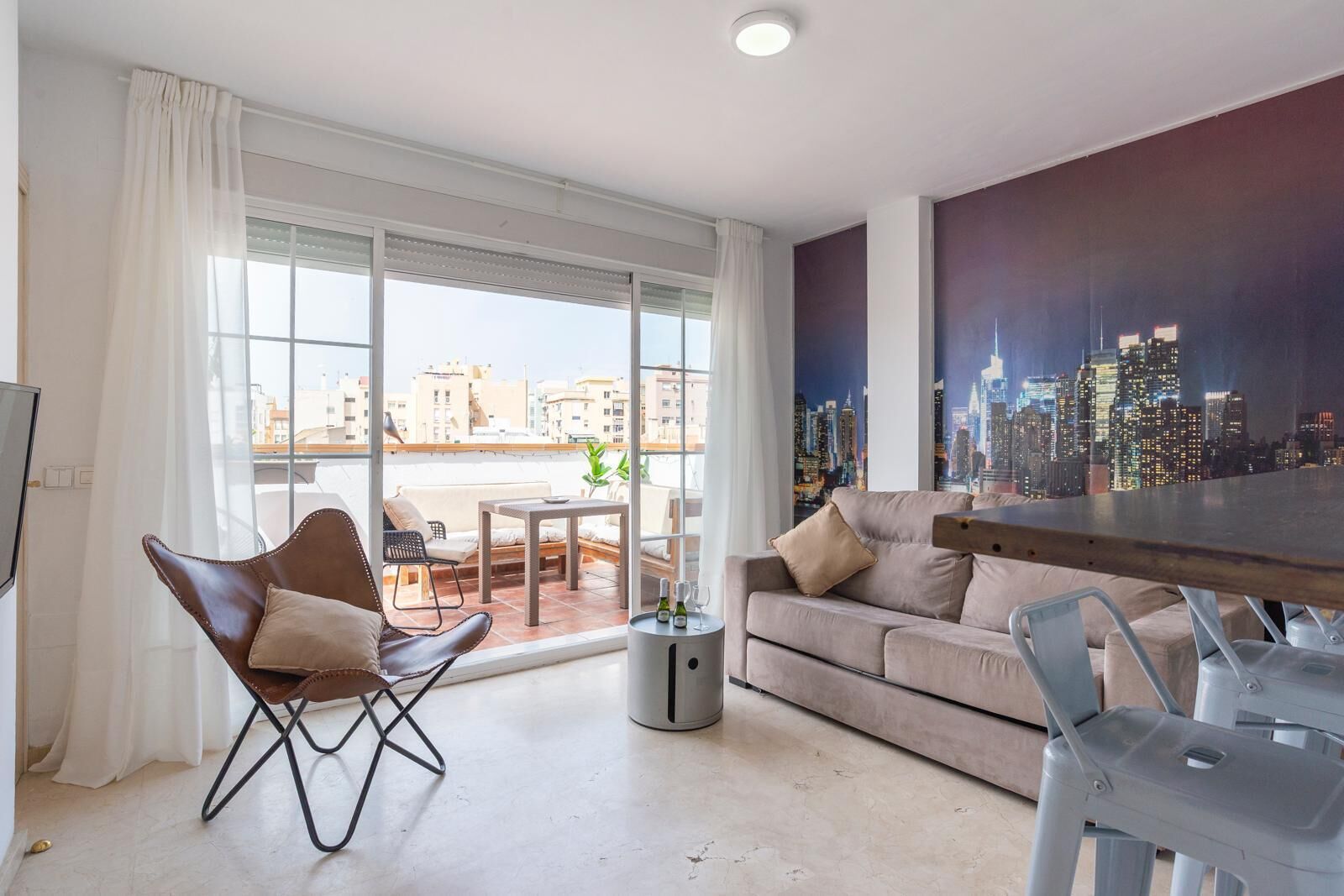 A modern living room with a sofa, a chair, a dining table, and a cityscape view through large windows.