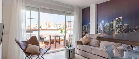A modern living room with a sofa, a chair, a dining table, and a cityscape view through large windows.
