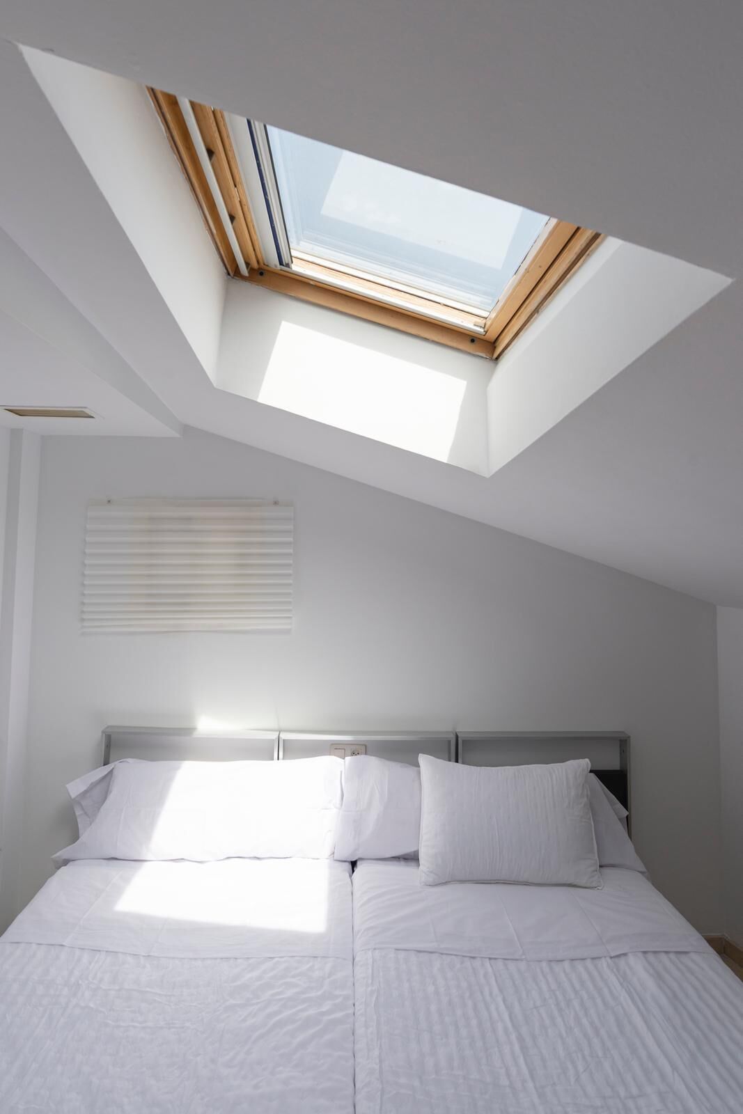 A bedroom with a skylight, a bed with white bedding, and a headboard.