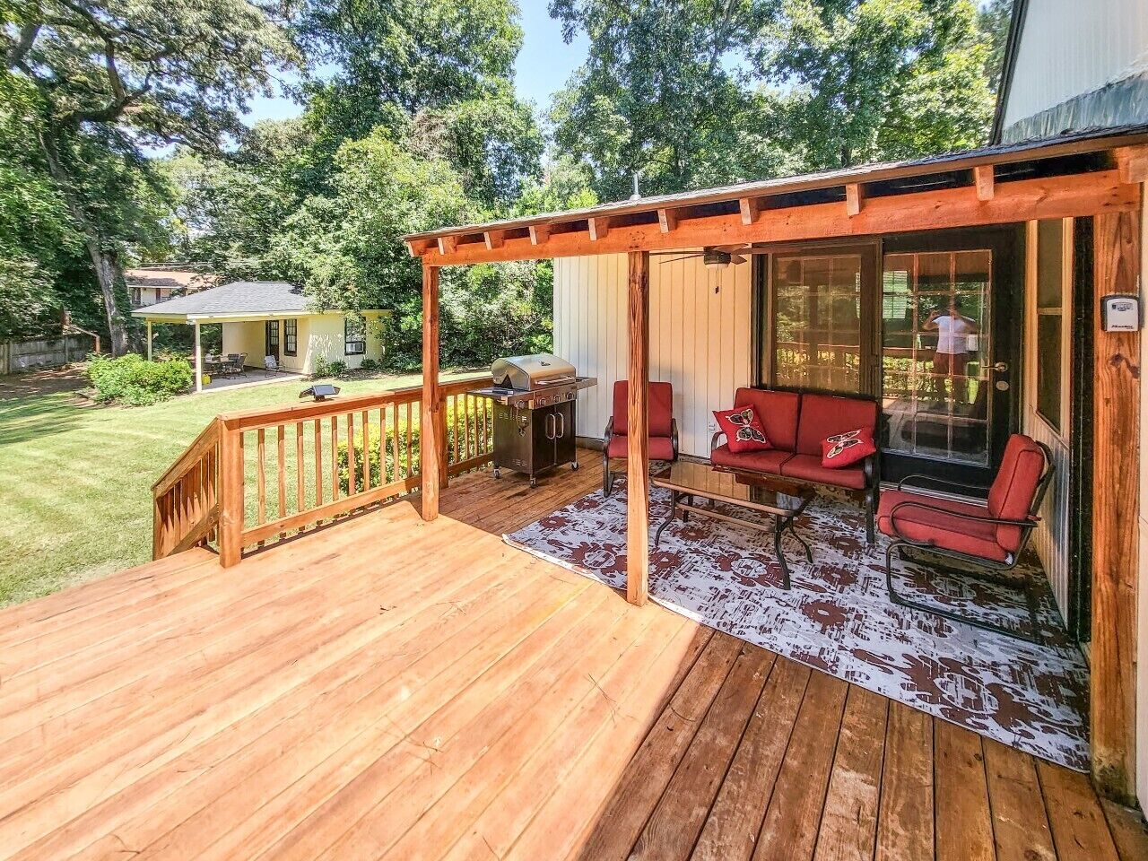 A wooden deck with a covered seating area, a grill, and a view of the surrounding greenery.