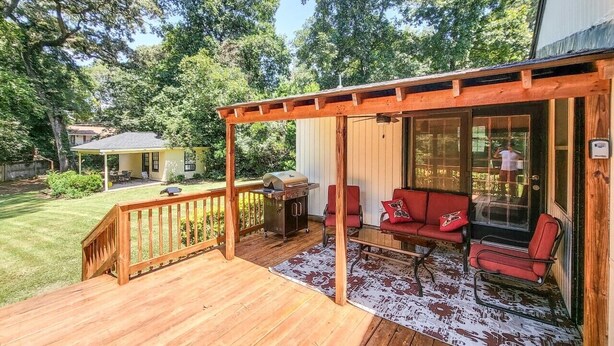A wooden deck with a covered seating area, a grill, and a view of the surrounding greenery. - 5-Bedroom, 3-Bathroom Cozy Home (Warner Robins)
