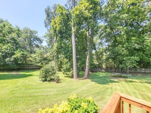 A grassy backyard with trees, a wooden deck, and a trampoline. - 5-Bedroom, 3-Bathroom Cozy Home (Warner Robins)