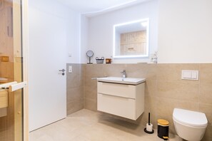 Un baño moderno con lavamanos, espejo e inodoro blancos.
