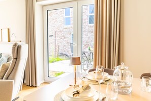 A dining area with a table set for two, a lamp, and a view of a brick building through a glass door. - Beach Loft – Close to the beach. Sauna. Patio. Dogs are welcome. (Tossens)