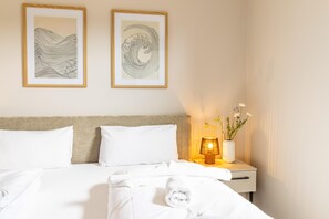 A hotel room with a bed, two framed artworks on the wall, a bedside table with a lamp and flowers, and a neatly made bed with a towel. - Beach Loft – Close to the beach. Sauna. Patio. Dogs are welcome. (Tossens)