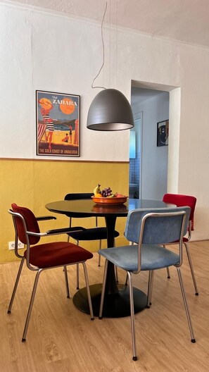 A dining area with a round table, four chairs, a fruit bowl, and a pendant light. - Quiet Apartment with Pool & Rooftop Terrace – Conil de la Frontera (Conil de la Frontera)