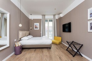 Ein modernes Schlafzimmer mit Bett, Sessel, Fernseher und einem Fenster mit Vorhängen.
