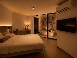 Ein Schlafzimmer mit Bett, Nachttisch, Lampe und einem an der Wand befestigten Fernseher.