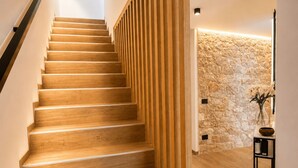A wooden staircase with a modern design, leading to a room with a stone wall and a small table with a vase and a bowl. - NEW: Casa Serenia - Residence Corte Carden 2 (Bardolino)