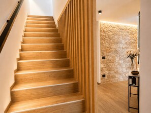 A wooden staircase with a modern design, leading to a room with a stone wall and a small table with a vase and a bowl. - NEW: Casa Serenia - Residence Corte Carden 2 (Bardolino)